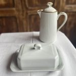 Beurrier en faïence blanche Pillivuyt Beurrier ancien chic de Méhun-sur-Yèvre Il y a des maisons qui traversent les siècles sans perdre leur âme. Pillivuyt en fait partie. Ce beurrier en faïence blanche, sobre et élégant, incarne parfaitement cet esprit : une vaisselle pensée pour durer, belle sans en faire trop, et toujours juste sur une table. Dans cette nouvelle sélection, j’ai eu envie de remettre les beurriers à l’honneur. Et celui-ci, avec son blanc lumineux et ses lignes intemporelles, s’impose comme un beau classique. • de 300 avis clients satisfaits certifiés par avis garantis ⸻ Description du beurrier blanc Pillivuyt Ce beurrier est réalisé en faïence blanche, dans un style épuré qui fait toute sa force. Le blanc traverse les modes, s’accorde avec toutes les vaisselles, et apporte cette impression de table soignée, sans jamais en faire trop. C’est un beurrier ancien de la maison Pillivuyt, une référence française dans l’univers de la céramique culinaire. Une pièce à la fois utile et décorative, qui trouve naturellement sa place sur une table du quotidien comme sur une table de fête. ⸻ Dimensions • Longueur : 18 cm • Largeur : 12 cm • Hauteur : 9 cm Un format idéal pour accueillir une motte de beurre et servir facilement à table. ⸻ État Le beurrier est en parfait état. Aucun éclat. Aucune fêle. Une très belle pièce, prête à être utilisée. ⸻ Prix et livraison 💶 Prix de vente : 20 euros 📦 Livraison possible par : • Mondial Relais • Colissimo Partout en France. ⸻ La faïence blanche, élégance du quotidien La faïence est une céramique recouverte d’un émail qui lui donne cet aspect lisse et lumineux. Depuis des siècles, elle accompagne les tables françaises. Elle est solide, agréable à l’usage, et elle supporte parfaitement la vie de tous les jours. La faïence blanche a ce pouvoir particulier : elle met en valeur ce que l’on sert. Le beurre paraît plus doré. Le pain plus appétissant. Et la table, tout simplement, plus belle. ⸻ Pillivuyt, un grand nom de la céramique française La maison Pillivuyt est fondée en 1818 à Méhun-sur-Yèvre, dans le Cher, au cœur de la France. Dès l’origine, l’entreprise se spécialise dans la fabrication de vaisselle en céramique de haute qualité, destinée aussi bien aux particuliers qu’aux professionnels. Au fil du XIXᵉ siècle, Pillivuyt développe un savoir-faire unique et met au point une porcelaine culinaire extrêmement résistante, parfois décrite comme une porcelaine hybride. Elle supporte : • les chocs thermiques, • les hautes températures du four, • les usages intensifs de la restauration et de l’hôtellerie. C’est cette robustesse, alliée à une grande élégance, qui fait la réputation de la marque. Très tôt, les pièces Pillivuyt équipent les grandes tables, les hôtels et les restaurants exigeants. Deux siècles plus tard, la manufacture est toujours installée à Méhun-sur-Yèvre. Elle incarne un véritable patrimoine industriel et artisanal français, reconnu pour la qualité et la longévité de ses productions. Posséder une pièce Pillivuyt, c’est donc faire entrer chez soi un peu de cette histoire. ⸻ Pourquoi choisir ce beurrier Pillivuyt ? Choisir ce beurrier, c’est choisir : • une pièce issue d’un savoir-faire français du XIXᵉ siècle, • un beau classique blanc, chic et intemporel, • une vaisselle pensée pour durer dans le temps, • un objet utile et décoratif, • une touche d’élégance simple sur la table. C’est le genre d’objet que l’on garde longtemps. Et que l’on aime ressortir. ⸻ Mon avis de brocanteuse Je le dis souvent, et je le pense vraiment : la vaisselle blanche, c’est toujours une valeur sûre. Elle traverse les époques sans jamais se lasser. Elle va avec tout. Et elle donne tout de suite une allure soignée à la table. Un beurrier, en plus, c’est un détail qui change tout. C’est hyper chic au quotidien, et encore plus joli sur une table de fête. Pour moi, c’est un objet que l’on s’offre pour se faire plaisir, parce qu’on aime les belles choses simples. Ce beurrier Pillivuyt, je le trouve parfait pour ça. ⸻ Avis clients – La brocante bucolique.fr • de 300 avis clients satisfaits certifiés par avis garantis ⭐⭐⭐⭐⭐ “Objets toujours magnifiques et descriptions très fidèles. Un vrai plaisir.” – Claire ⭐⭐⭐⭐⭐ “Très belle vaisselle, envoi soigné. Je recommande sans hésiter.” – Sophie ⭐⭐⭐⭐⭐ “Des pièces pleines de charme et d’histoire. J’adore.” – Marc ⭐⭐⭐⭐⭐ “Chaque commande est une découverte. Merci pour ces trésors.” – Isabelle ⭐⭐⭐⭐⭐ “Service parfait et objets superbes pour ma table.” – Julien ⸻ FAQ – Beurrier en faïence blanche Pillivuyt Ce beurrier est-il ancien ? Oui, il s’agit d’un beurrier ancien de la maison Pillivuyt, issue d’une production du XIXᵉ ou début XXᵉ siècle. Peut-on l’utiliser au quotidien ? Oui, il est parfaitement adapté à un usage quotidien comme aux repas de fête. Qu’est-ce qui fait la réputation de Pillivuyt ? Pillivuyt est reconnue depuis 1818 pour sa porcelaine culinaire très résistante, utilisée dans l’hôtellerie et la restauration. La faïence est-elle solide ? Oui, surtout chez Pillivuyt, où la vaisselle est pensée pour durer et supporter un usage intensif. Le beurrier est-il en bon état ? Oui, il est en parfait état, sans éclat ni fêle. Est-ce un bel